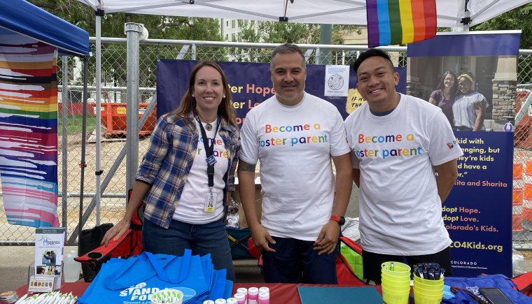 Three adults at an event table promoting becoming a foster parent