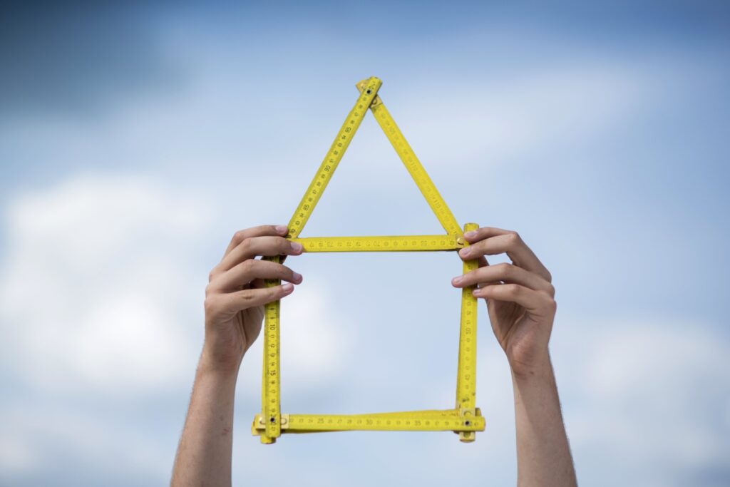 Two hands hold up connected rulers that form the outline of a house.