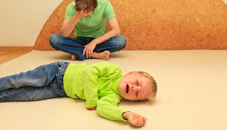 A toddler in a green shirt throwing a tantrum on the floor.