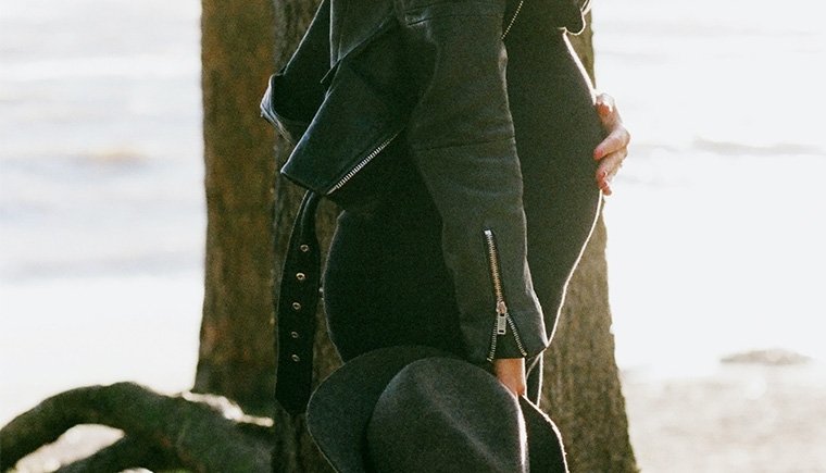 Woman in all black side view with a hand resting on her pregnant belly.
