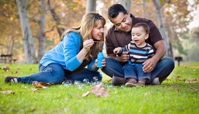 Two parents and a baby blowing bubble in a park.