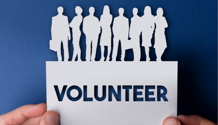 Person holding a piece of paper with the word volunteer cut out and a group of cut out people on the top.