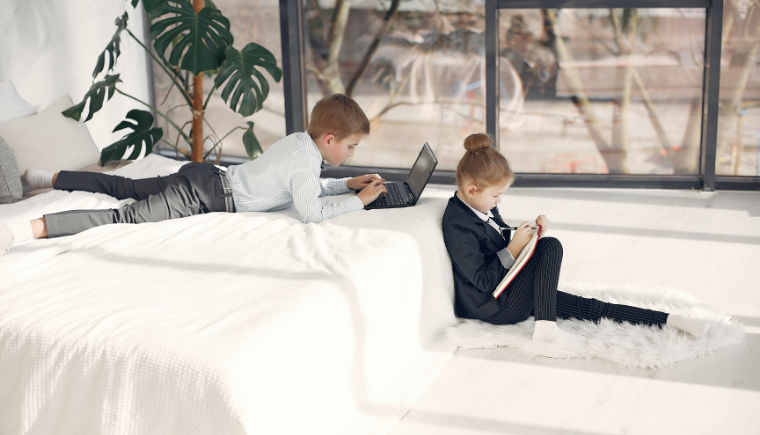 Two kids in their parents bedroom remote learning and wearing business suites.