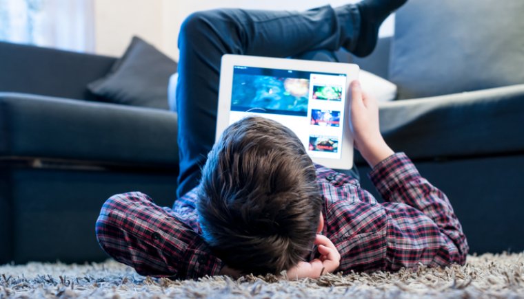 Youth laying on floor in living room watching shows on their tablet.