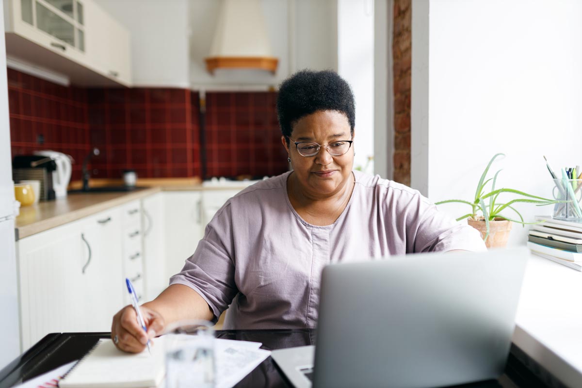 Woman wearing glasses taking notes in front of a laptop in a kitchen