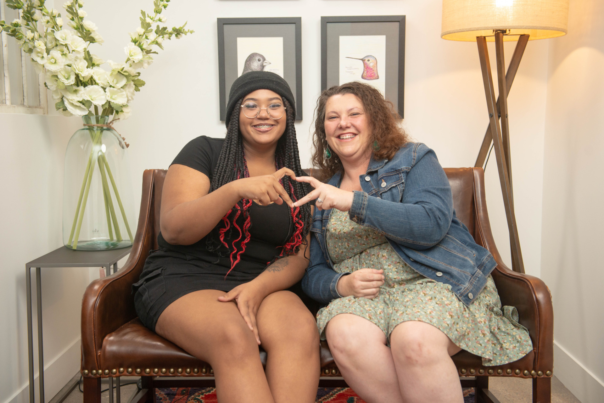 An adoptive mother and daughter sitting on the couch making a heart with their hands