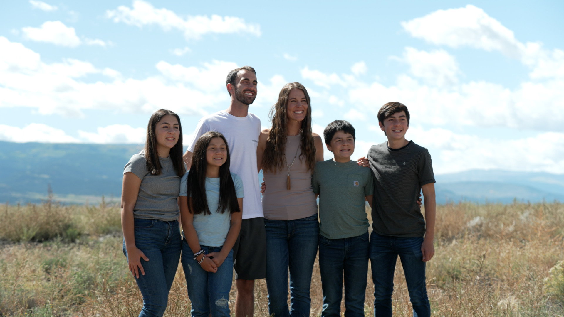 Family of six smiling with a mountain background