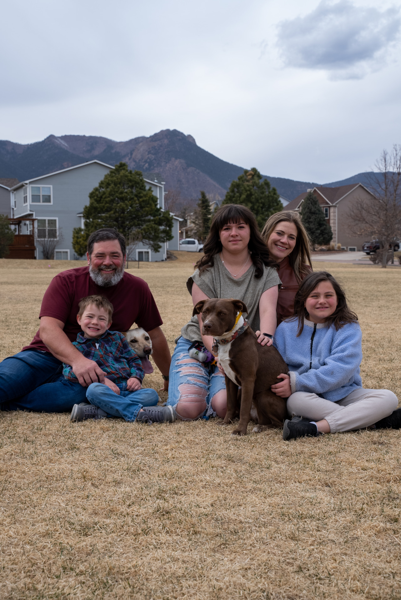 Una familia de crianza de Colorado de cinco miembros sentada en el parque con sus dos perros.