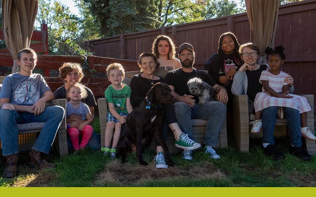 Una familia adoptiva de diez personas se sientados en su patio trasero con sus dos perros.