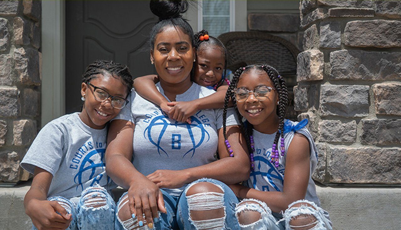 Una madre adoptiva soltera con sus tres hijas sonriendo en los escalones de la entrada de su casa.