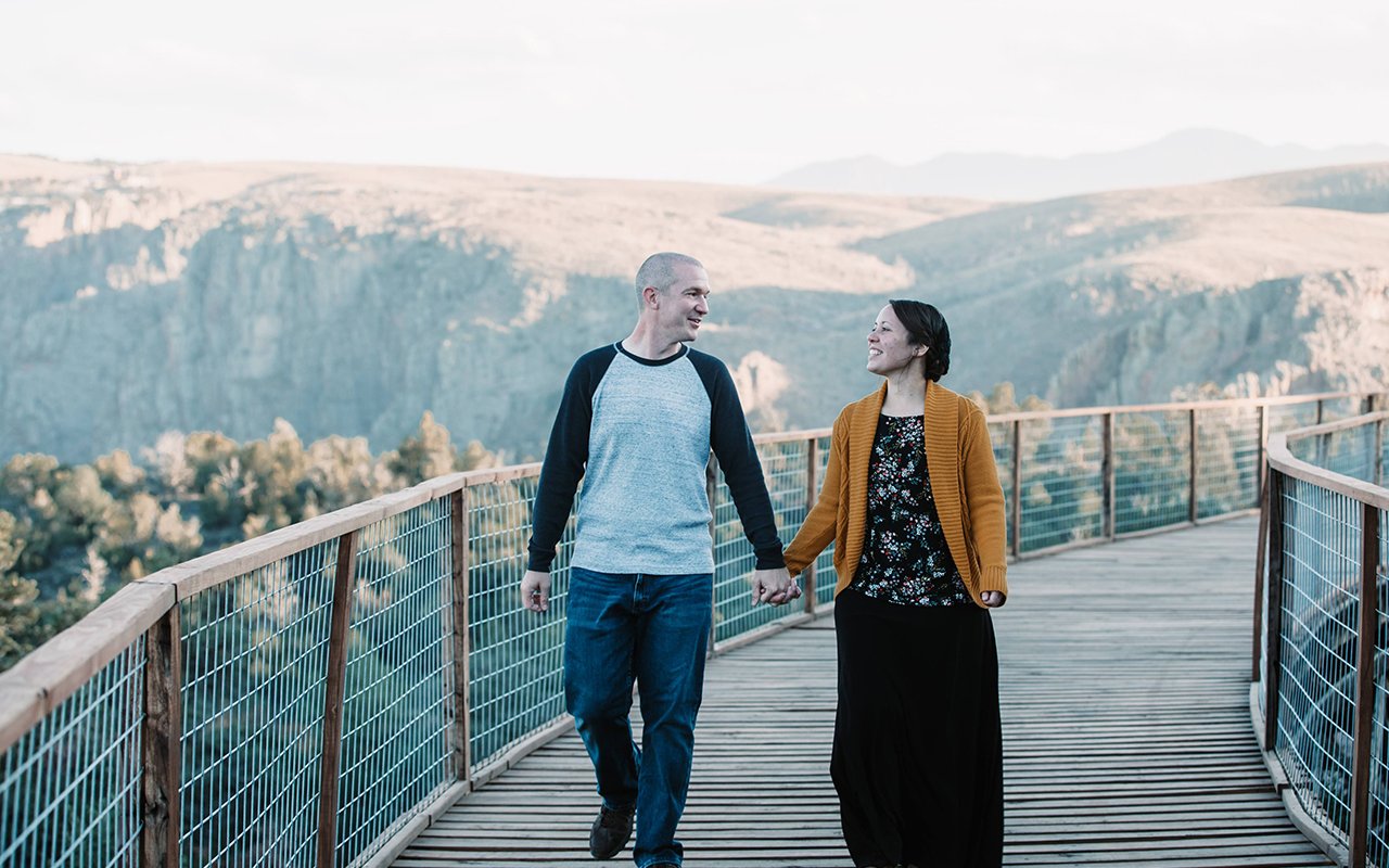 Una pareja se mira románticamente a los ojos mientras camina por una plataforma de observación en un punto escénico de Colorado.