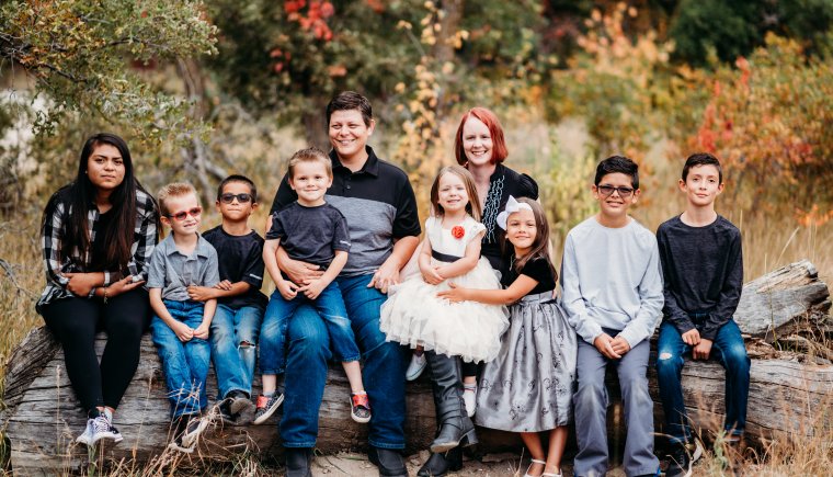 Una familia adoptiva de Colorado de diez personas posando para una foto familiar en un campo.