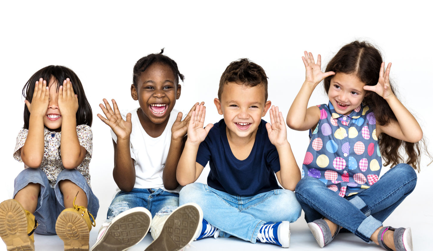 Cuatro niños de primaria haciendo caras graciosas mientras están sentados en el piso.