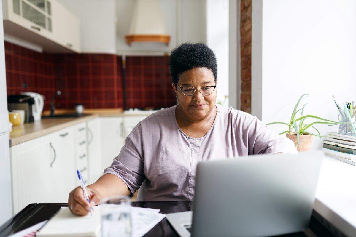 Mujer con gafas tomando notas frente a una computadora portátil en una cocina