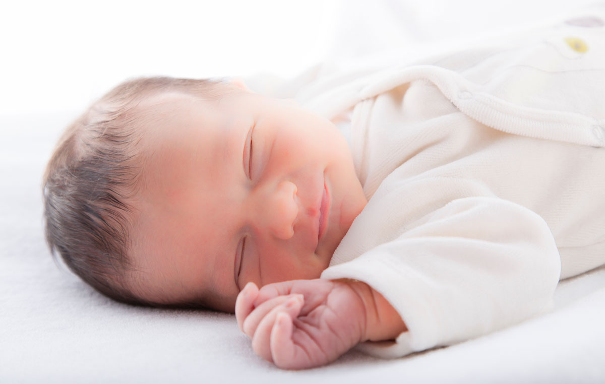 Un bebé duerme en su cuna con la mano junto a su cara.