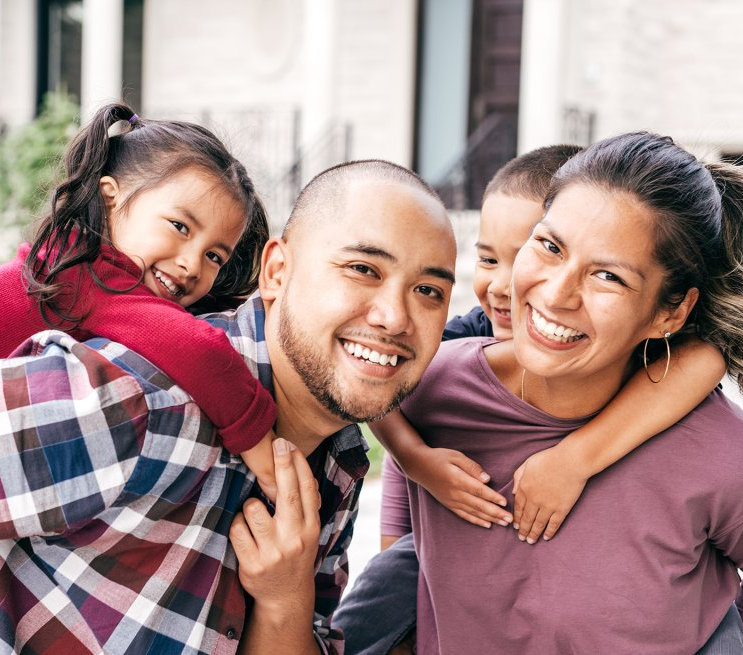 Dos padres sonrientes paseando sobre sus espaldas a sus hijos pequeños.