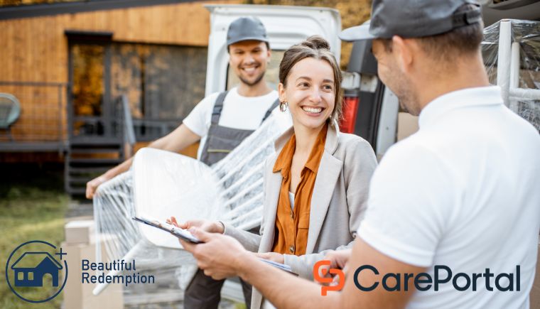 Two men, one with a clipboard, delivering furniture out of a truck to a woman.