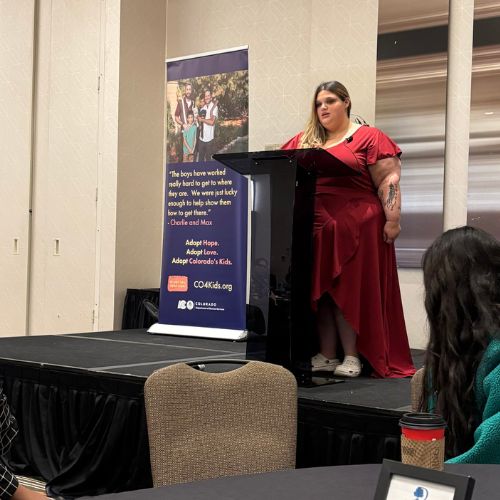 Young woman with long hair in a dress stands at a podium delivering a speech.